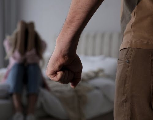 A woman cowering on the bed due to domestic violent abuse from her spouse.