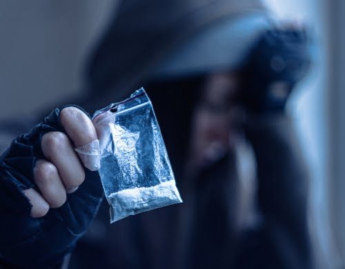 A man who is going to need a bail bond holding up a bag of powdered drugs he is selling.