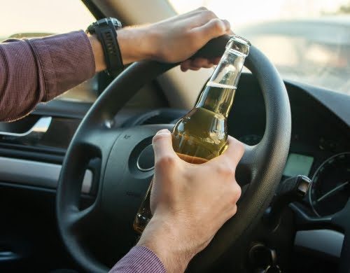 Man driving while holding an open container bottle in the car.